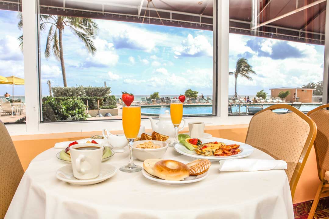 Picture of the ocean terrace, a table with plates and breakfast served, mimosas coffee cups bread, bagel, toasted bread, omelets, cereal, and fruits.